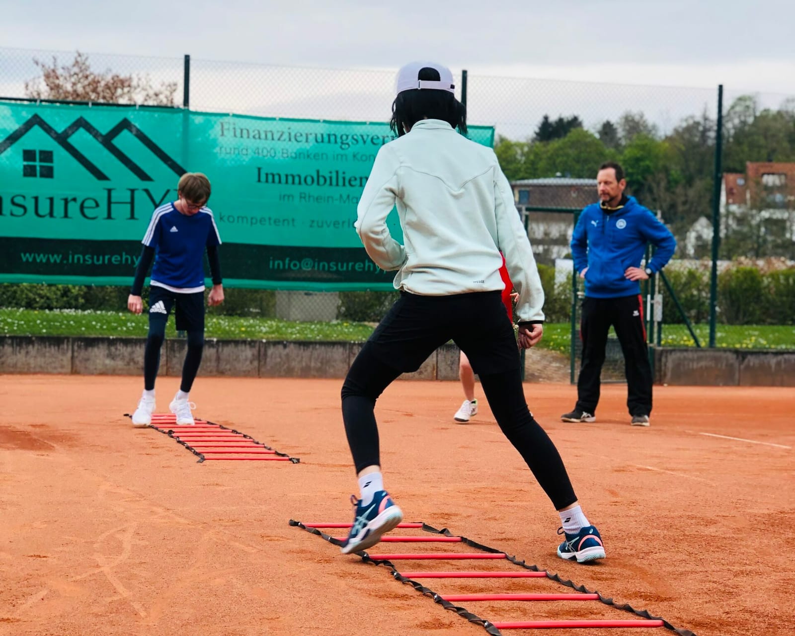 Koordinationstraining mit Leiter auf dem Sandplatz, Trainer im Hintergrund